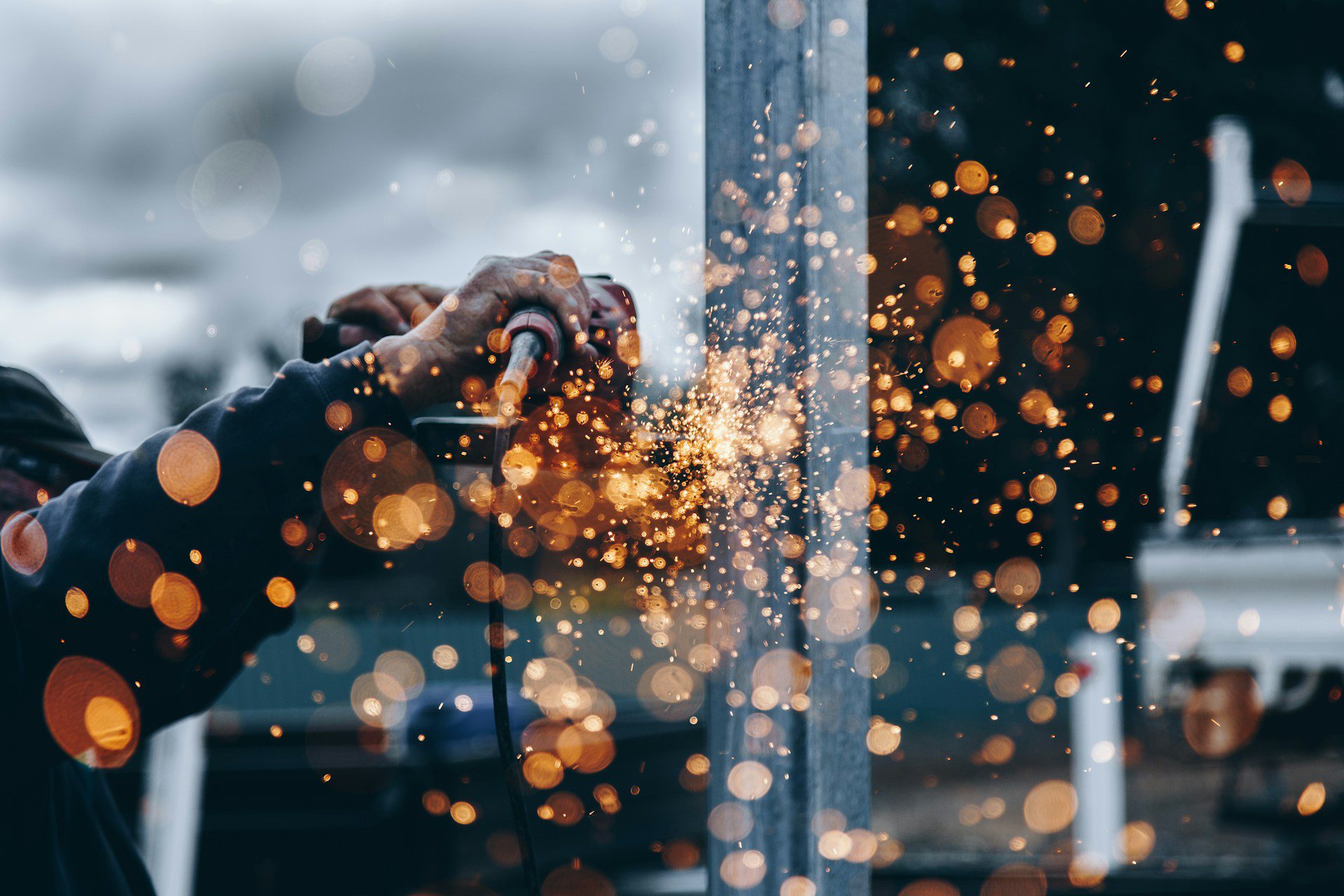 A person uses a grinder on metal, sending bright orange sparks flying against a blurred background, showcasing how innovation can reduce admin in construction safety without compromising efficiency.